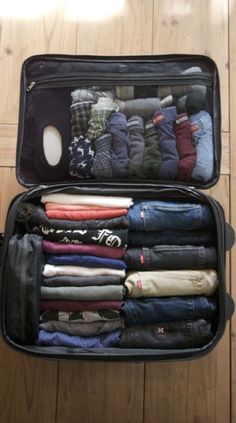 an open suitcase filled with clothes on top of a wooden floor