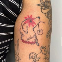 a woman's arm with tattoos on it and a dog holding a flower in its mouth