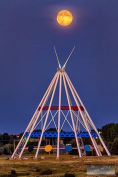 the full moon is setting over a tall structure with many poles and lights on it