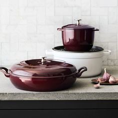 three pots and two pans are sitting on a counter top with garlic next to them