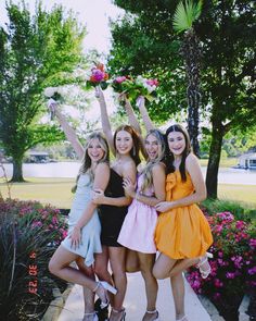 four young women posing for a photo in front of some trees and flowers with their arms up