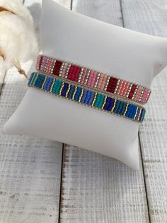 two bracelets sitting on top of a white pillow next to a piece of fabric