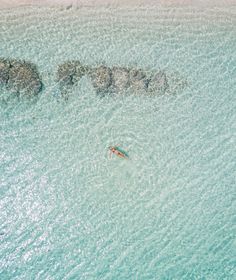 an aerial view of a person swimming in the ocean with rocks and water around them