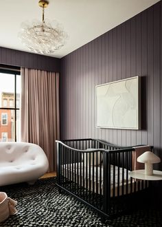 a baby's room with a white crib, black and white rug, chandelier and large window