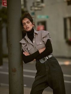 a woman leaning against a pole on the street