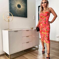 a woman in a dress standing next to a dresser