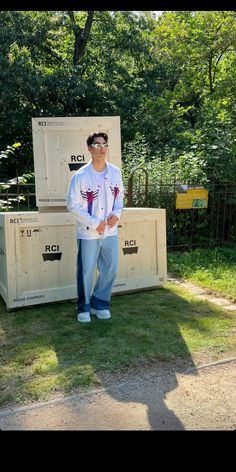 a man standing in front of two wooden crates on the grass with trees behind him