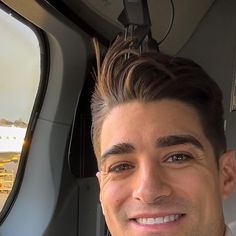 a young man is smiling while sitting in the passenger seat of an airplane and looking at the camera