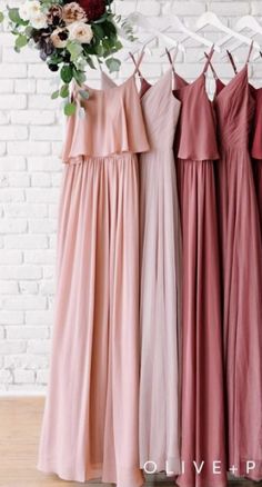 four bridesmaid dresses hanging up against a brick wall