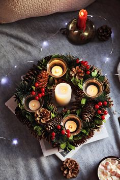 a christmas wreath with pine cones and candles on a bed next to other holiday decorations