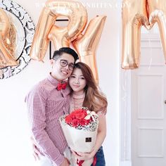 a man and woman standing next to each other in front of balloons that spell love