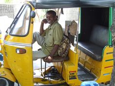 a man sitting in the driver's seat of a yellow vehicle talking on his cell phone