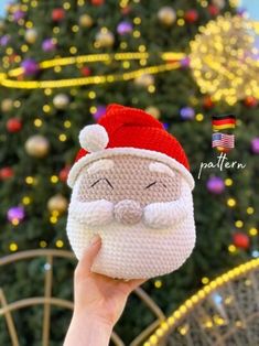 someone holding up a knitted santa clause ornament in front of a christmas tree