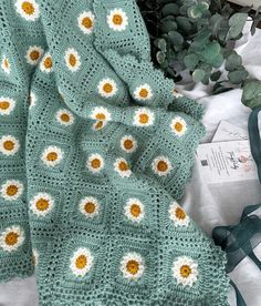 a crocheted blanket with yellow and white flowers on it next to a plant