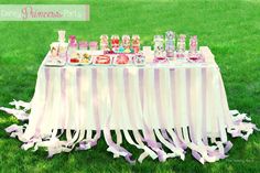 a table covered in candy on top of a lush green grass covered field with pink and white ribbons