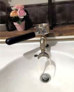 a close up of a faucet on a sink with flowers in the background