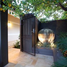 a gated entrance to a house with plants and trees in the foreground, next to a large potted planter