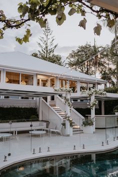 an outdoor swimming pool next to a white house with stairs leading up to the upper level