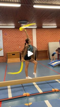 a woman in a gym holding a yellow frisbee and standing on a balance beam