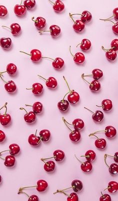 many cherries are scattered on a pink surface