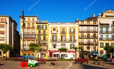 several buildings and benches in the middle of a plaza with people walking around them on a sunny day