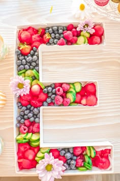 the letter e is made up of fruits and vegetables in white plastic containers on a table