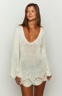 a woman wearing a white crochet sweater and short shorts, posing for the camera