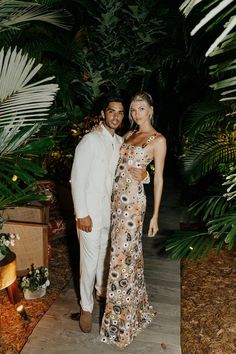 a man and woman standing next to each other in front of palm trees at night