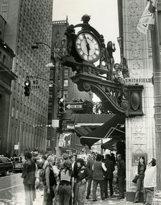 an old photo of people standing in front of a clock on the side of a building