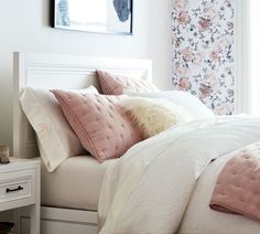 a bed with pink and white pillows on top of it next to a dresser in a bedroom