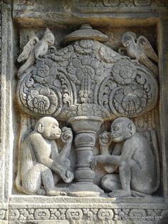 an intricately carved stone sculpture depicting monkeys and a vase with flowers on it's side