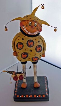 a wooden toy with an orange clown on it's head and legs, standing on a black base