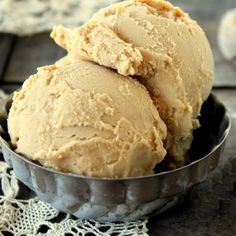 two scoops of ice cream sit in a metal bowl on a lace doily