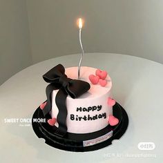 a white and black birthday cake with a single candle on top that says happy birthday