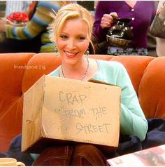 a woman sitting on a couch holding a cardboard box with the words crap from the street written on it