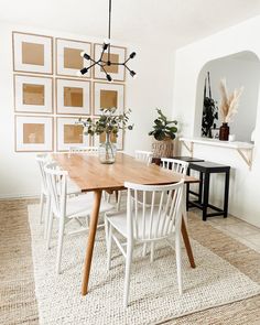 a dining room table with white chairs and pictures on the wall behind it, along with plants