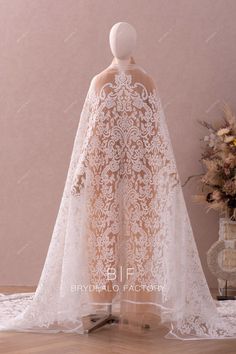 the back of a wedding dress with a cape on it, and flowers in the background