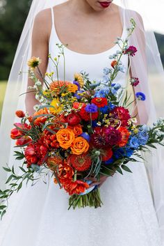 a woman in a wedding dress holding a bouquet of red, orange and blue flowers