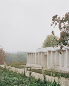 the building is white in color and has columns on both sides that are lined with grass