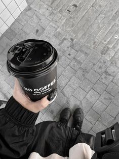 a person holding a cup of coffee in their hand while sitting on the ground with luggage