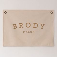 a white wall hanging with the name brady maxon in gold foil on it's side