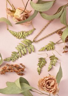 several different types of leaves and flowers on a pink surface with gold chain necklaces