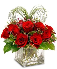 a vase filled with red roses and greenery