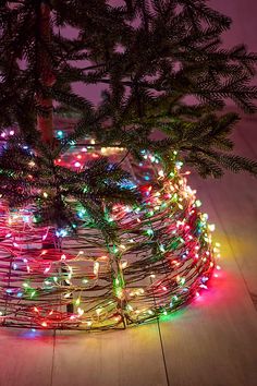 a small christmas tree with multicolored lights in a wire basket on a wooden floor