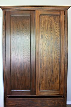 a wooden armoire with two doors on the top and bottom, sitting against a wall