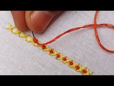 someone is stitching the thread on a piece of fabric with orange and yellow yarn