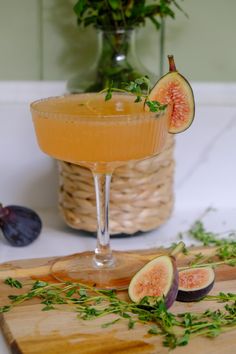 a glass filled with liquid and sliced figs on a cutting board next to a vase