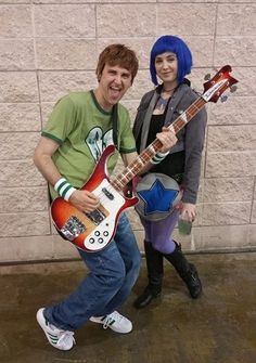 a man and woman are dressed up as rock band characters, one is holding an electric guitar