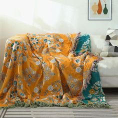 a couch covered in an orange and green blanket on top of a wooden floor next to a white sofa