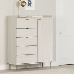 a white cabinet with five drawers and a gold lamp on top in a living room